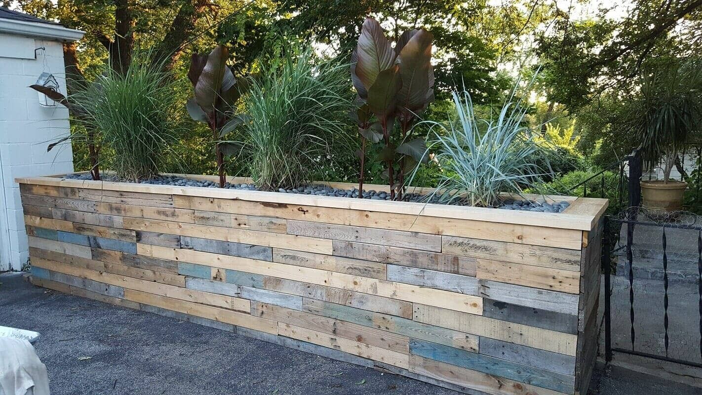 Long wooden planter wall with greenery and sculptures in a garden setting