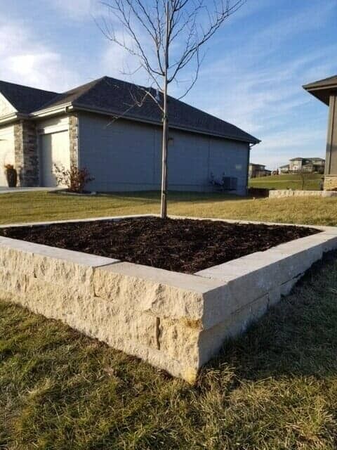 Raised stone planter bed with dark soil in a suburban yard beside a house