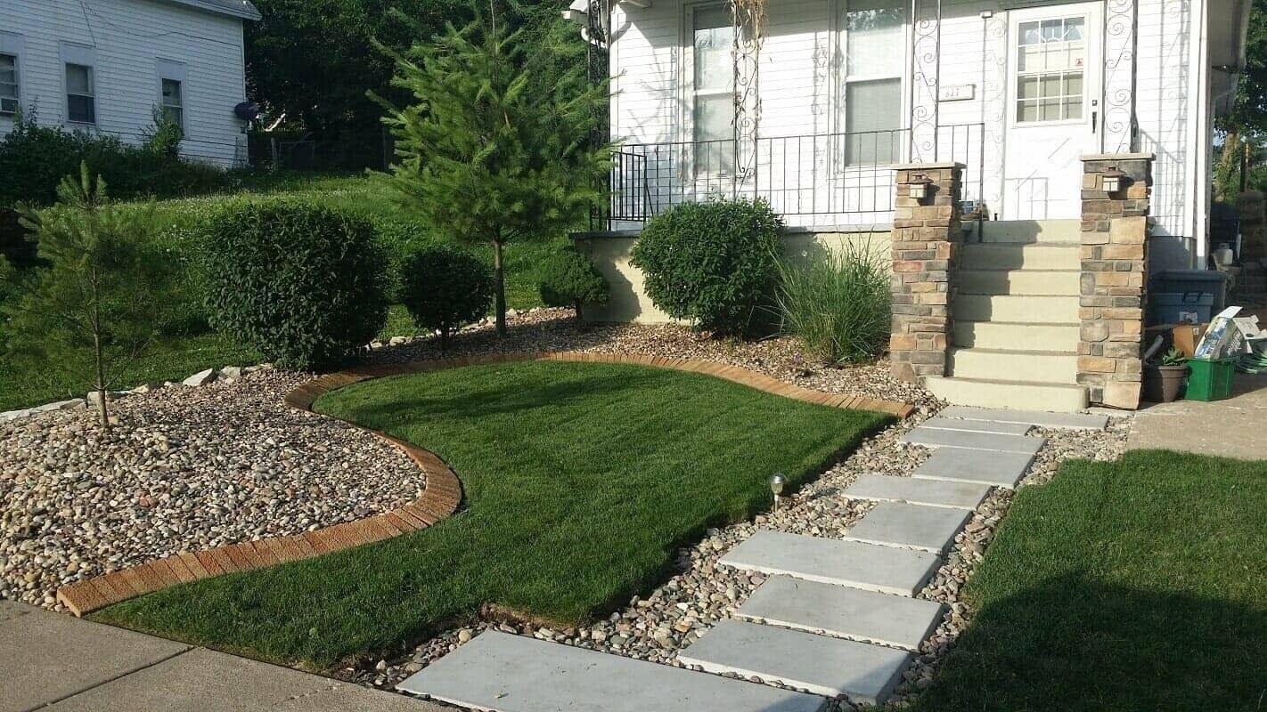 Front yard landscaping with stone path, green lawn, and front steps leading to a white house
