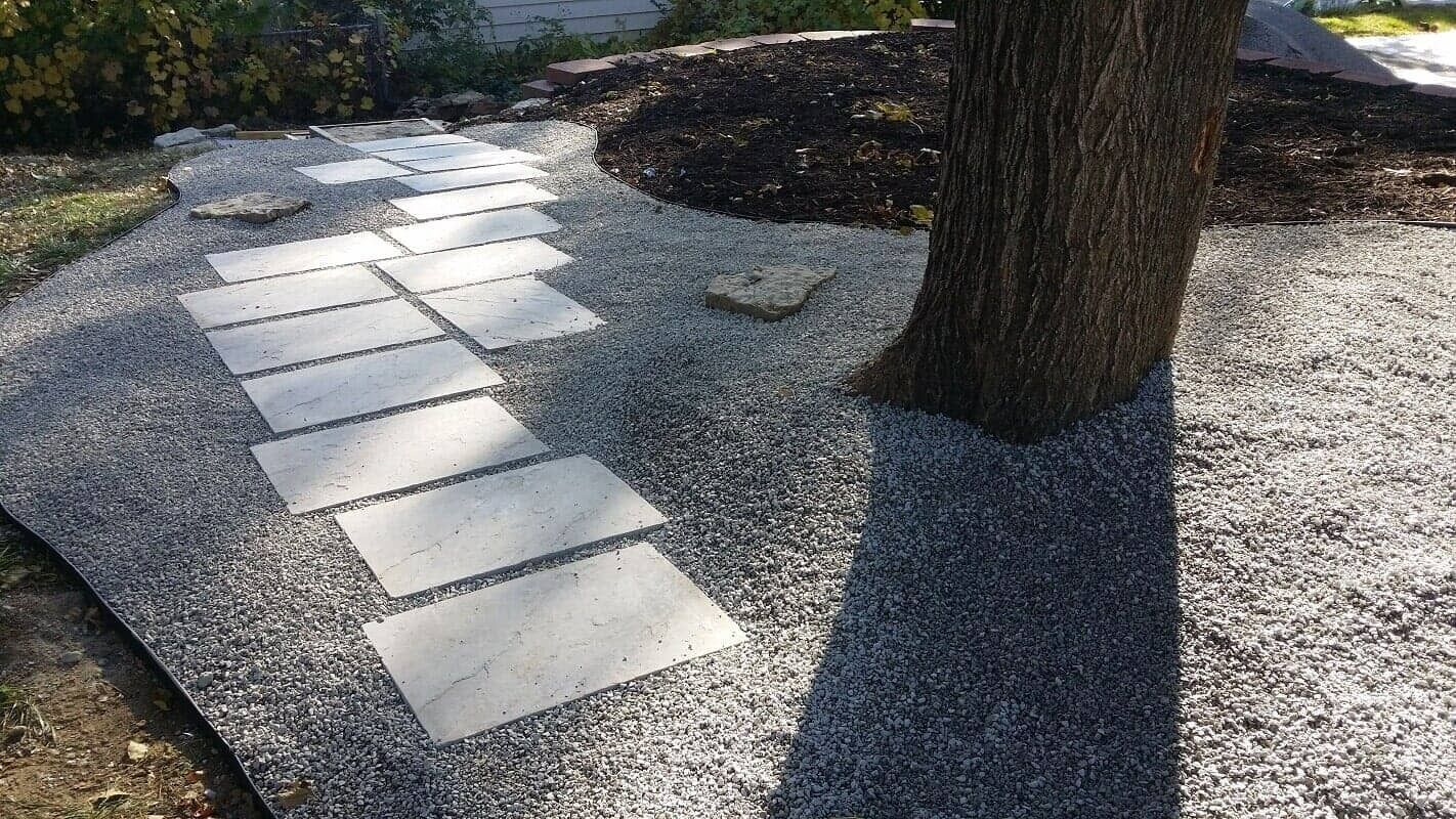 Curved stone stepping path through gray gravel around a large tree in a landscaped garden