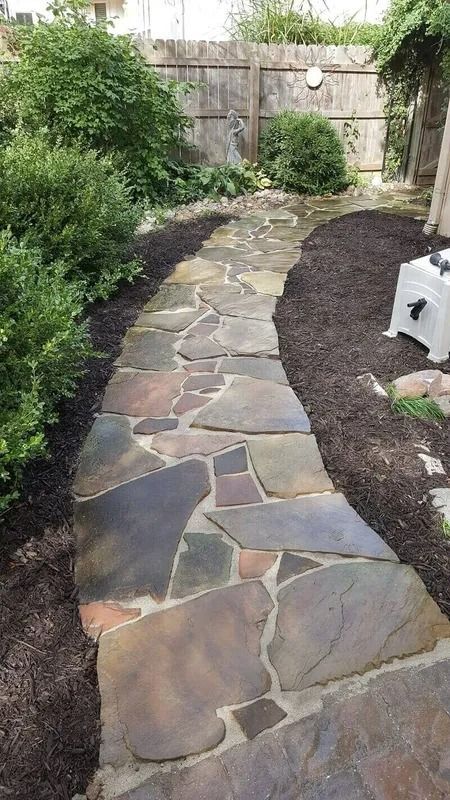 Stone garden path bordered by dark mulch and greenery leading to a fence