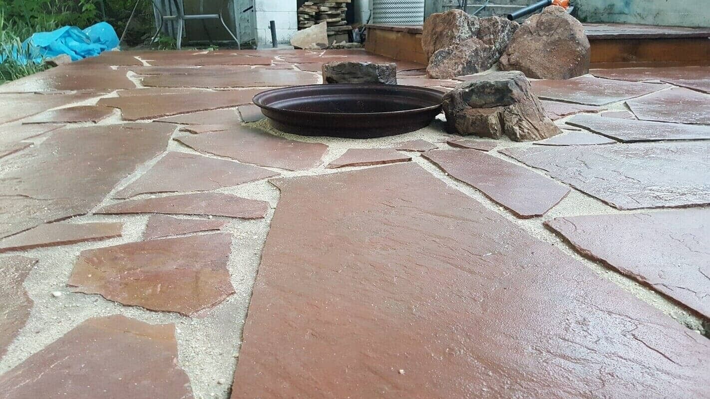 Stone patio with a black fire pit in the center and rocks along the edge