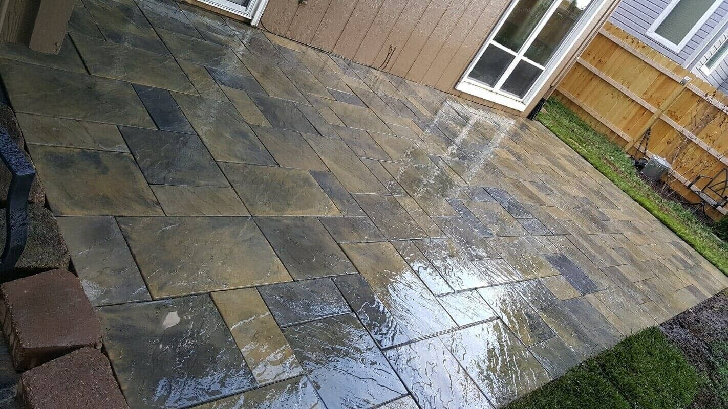Wet stone patio with puddles beside a wooden fence and brick wall.