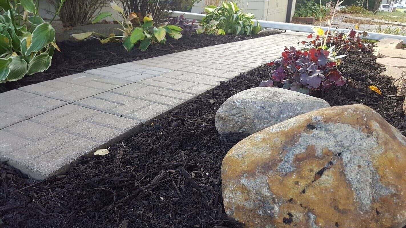 Stone garden path beside dark mulch, large rocks, and red-leaf plants in a landscaped yard