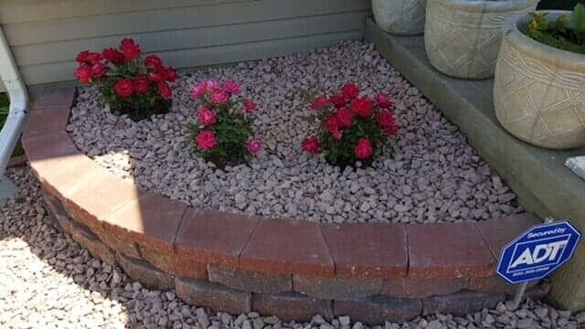 Small curved flower bed with red roses and gravel edging beside a house porch