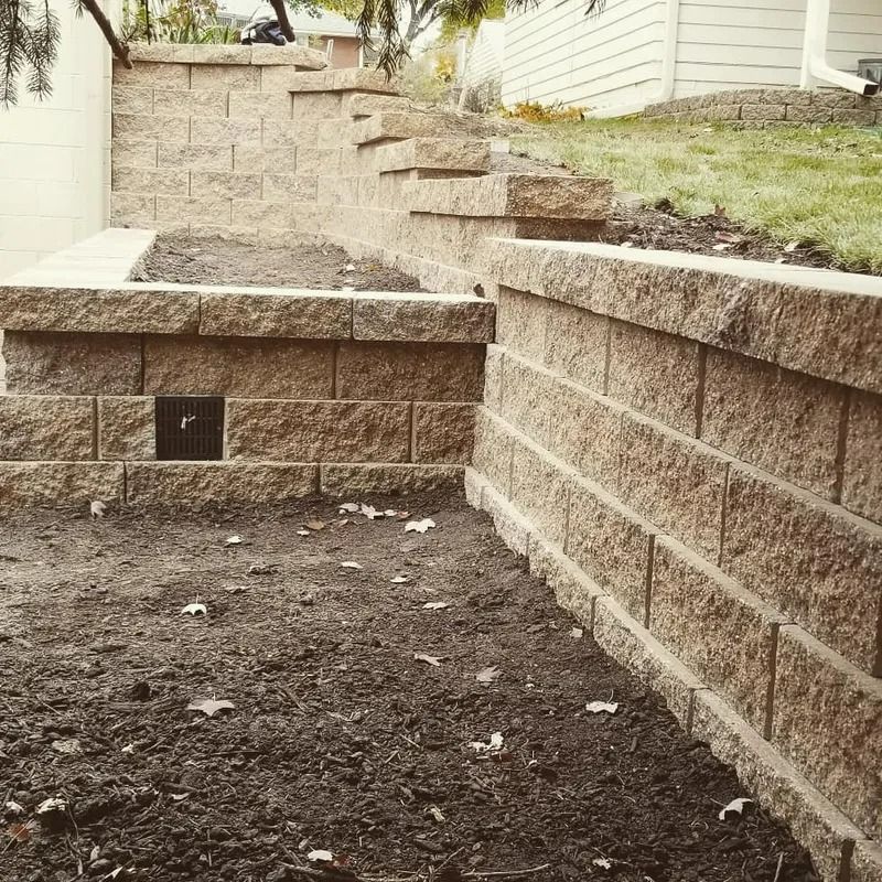 Stone retaining walls and steps beside a house, with a dirt patio area in front