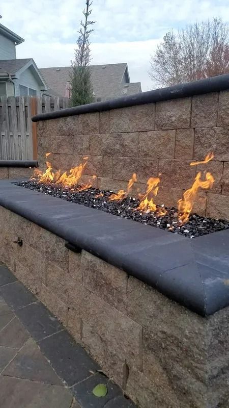 Outdoor stone fire feature with low orange flames along a backyard wall and bench seating