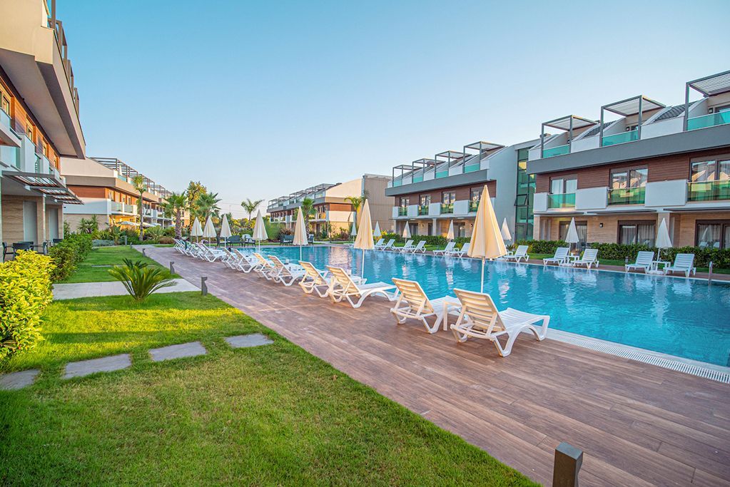 Lined pool with lounge chairs, surrounded by grass and multi-story buildings on a sunny day.