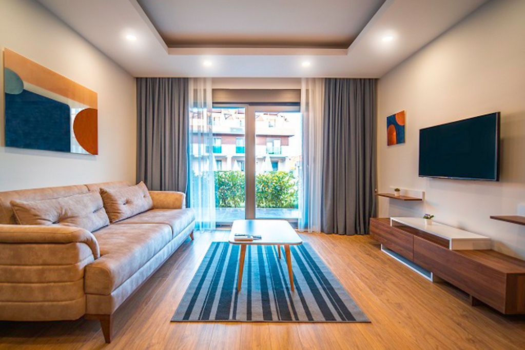 Living room with beige sofa, artwork, TV, and a balcony door; wooden floors.