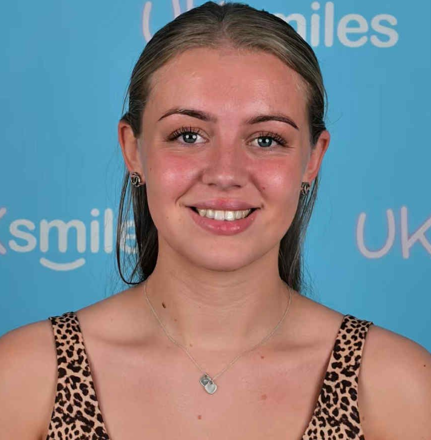 Woman with fair skin smiles at the camera, wearing animal print top and a necklace, against a blue background.
