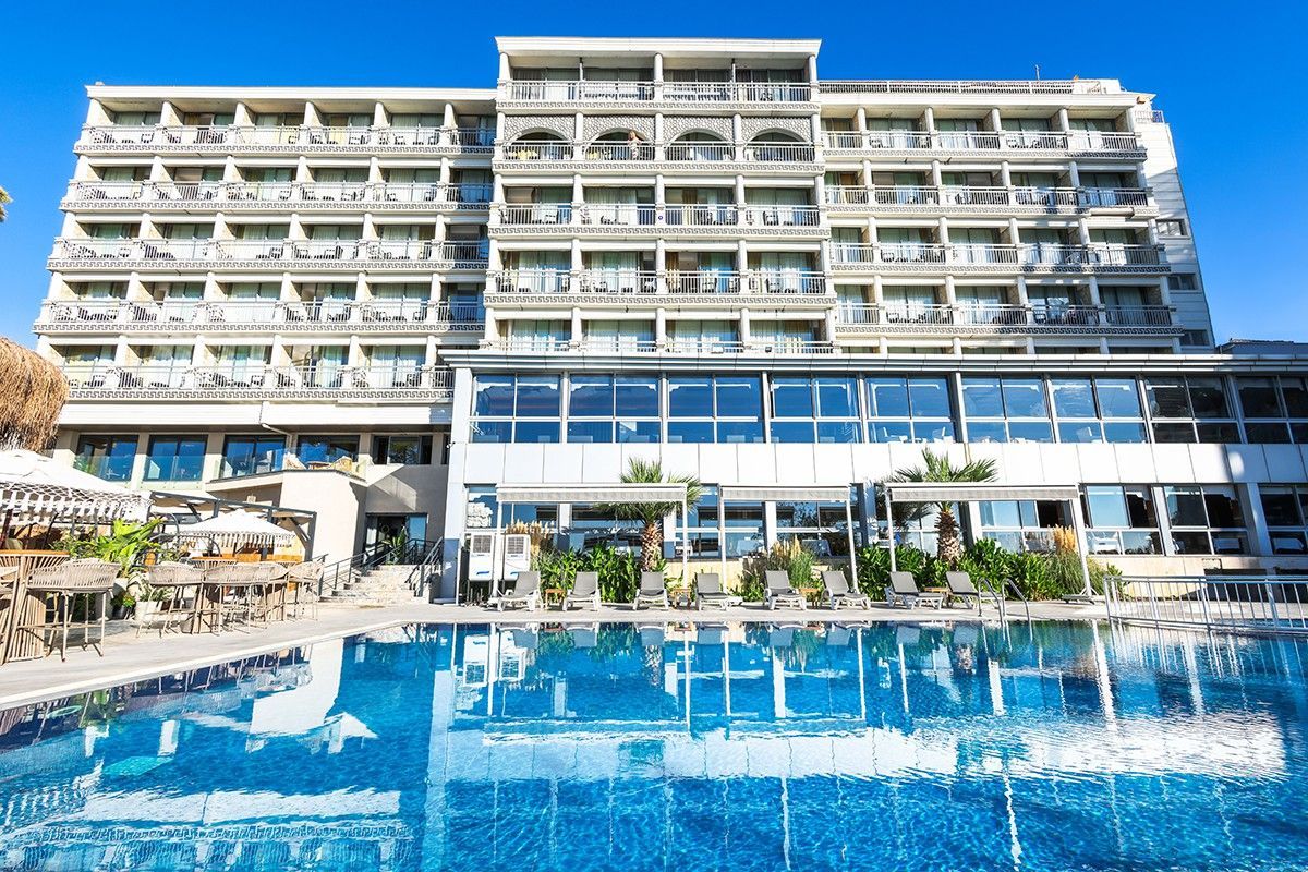 Hotel with a pool on a sunny day. Blue water and sky, building with balconies.