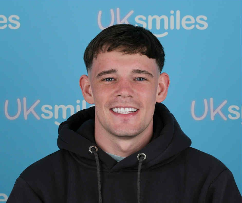 Man with short dark hair and a black hoodie smiling at the camera, against a blue backdrop.