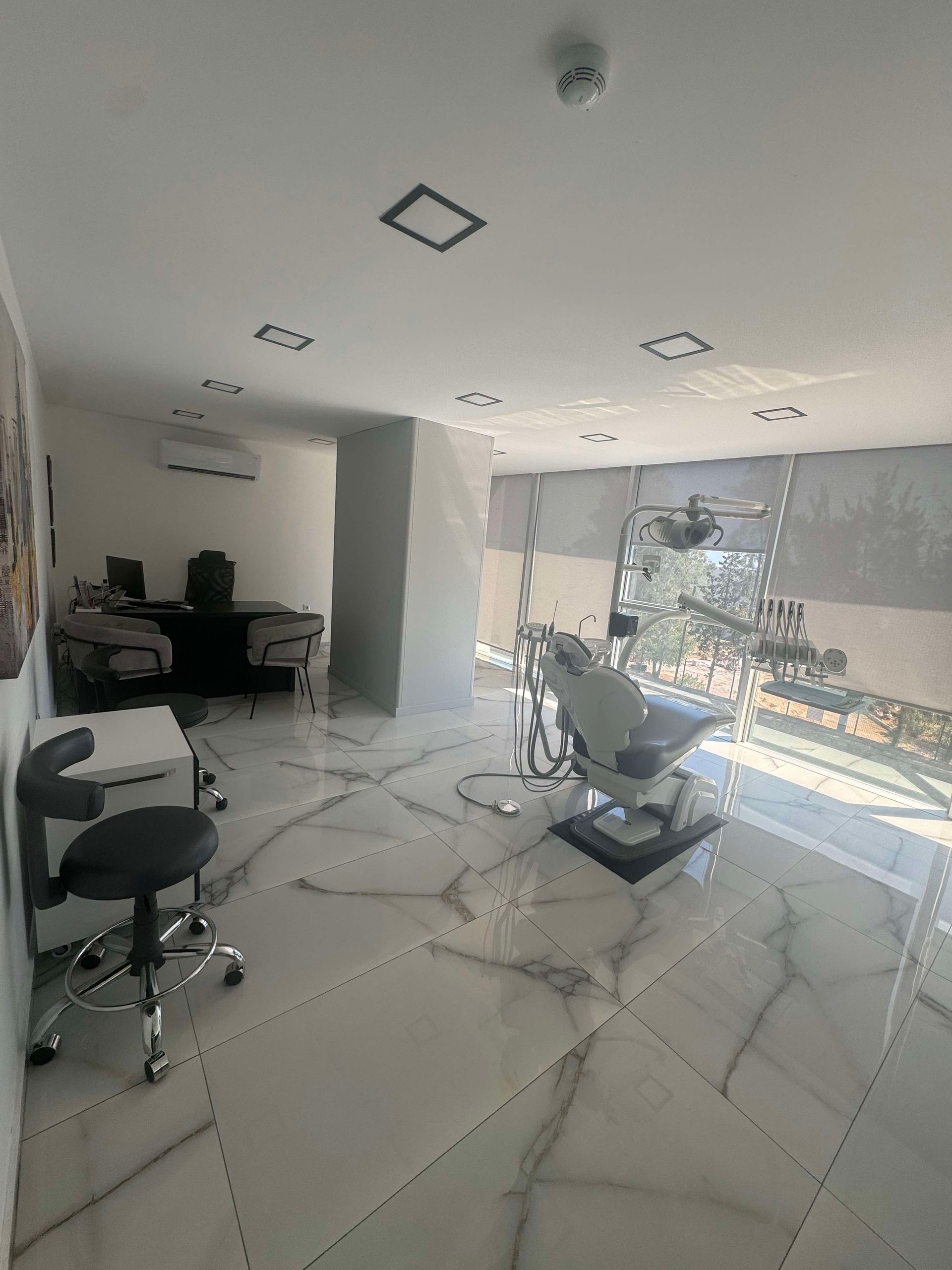 Dental office with a dental chair, black stool, and marble floor.