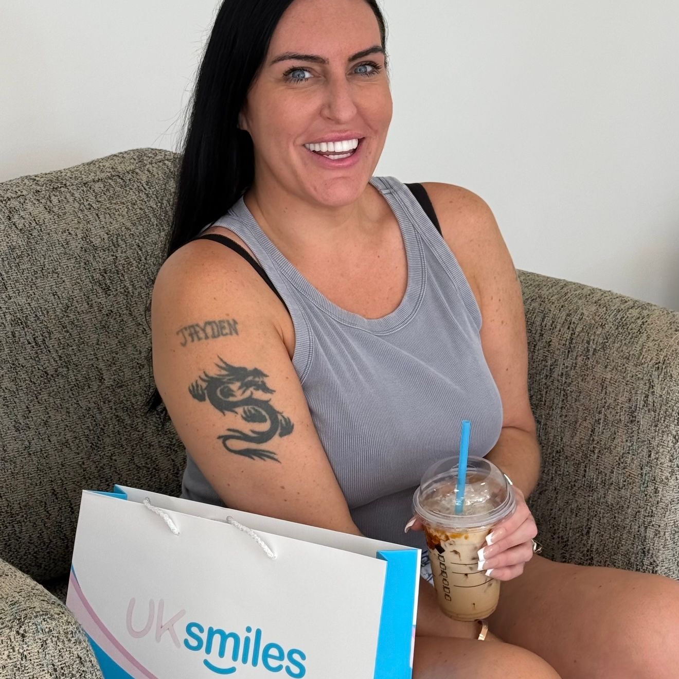 Woman with a dragon tattoo, smiling, holding an iced coffee and a shopping bag that says