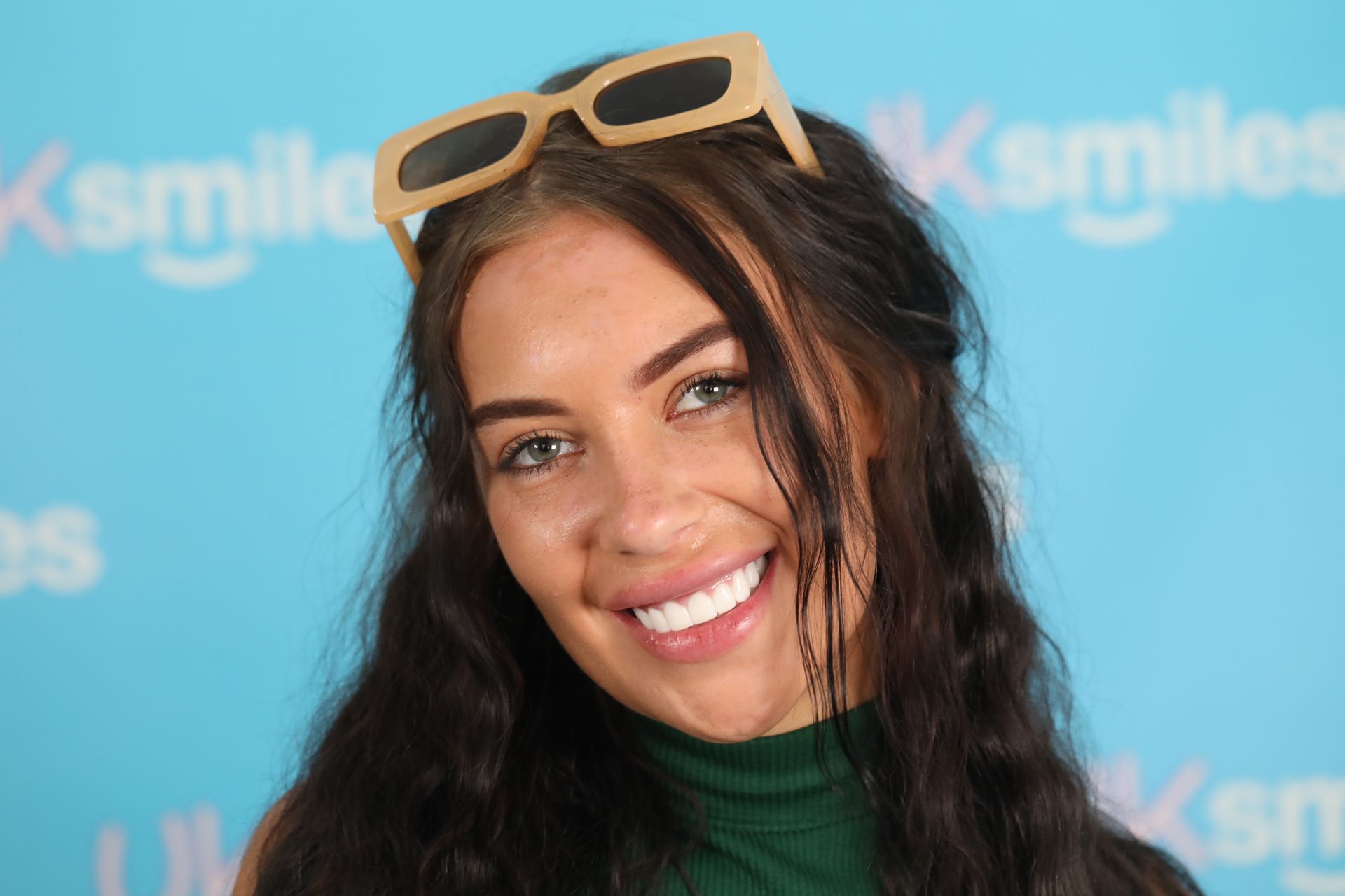 Woman with sunglasses on head smiling, blue background,