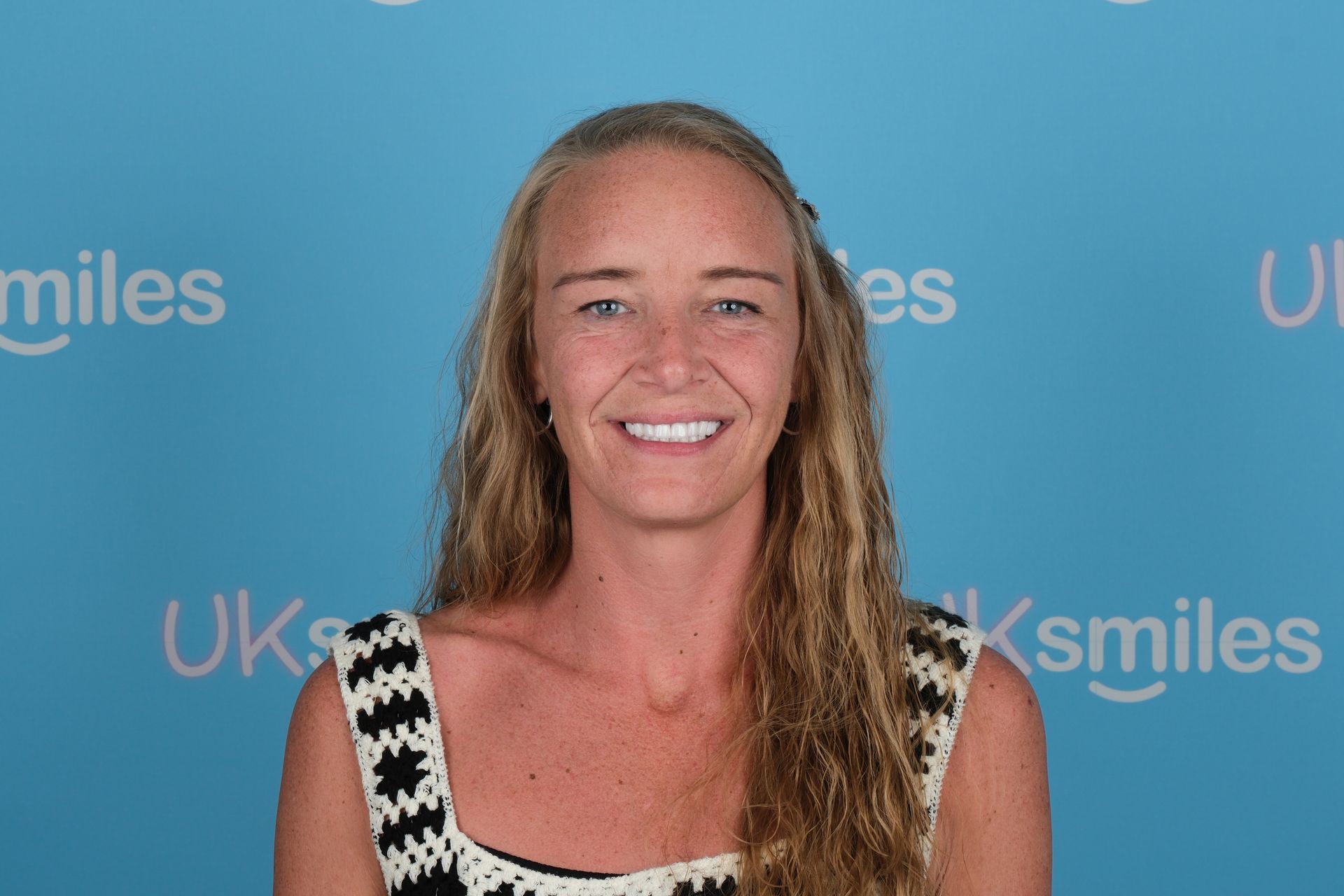 Woman with long blonde hair smiles at the camera against a blue backdrop with