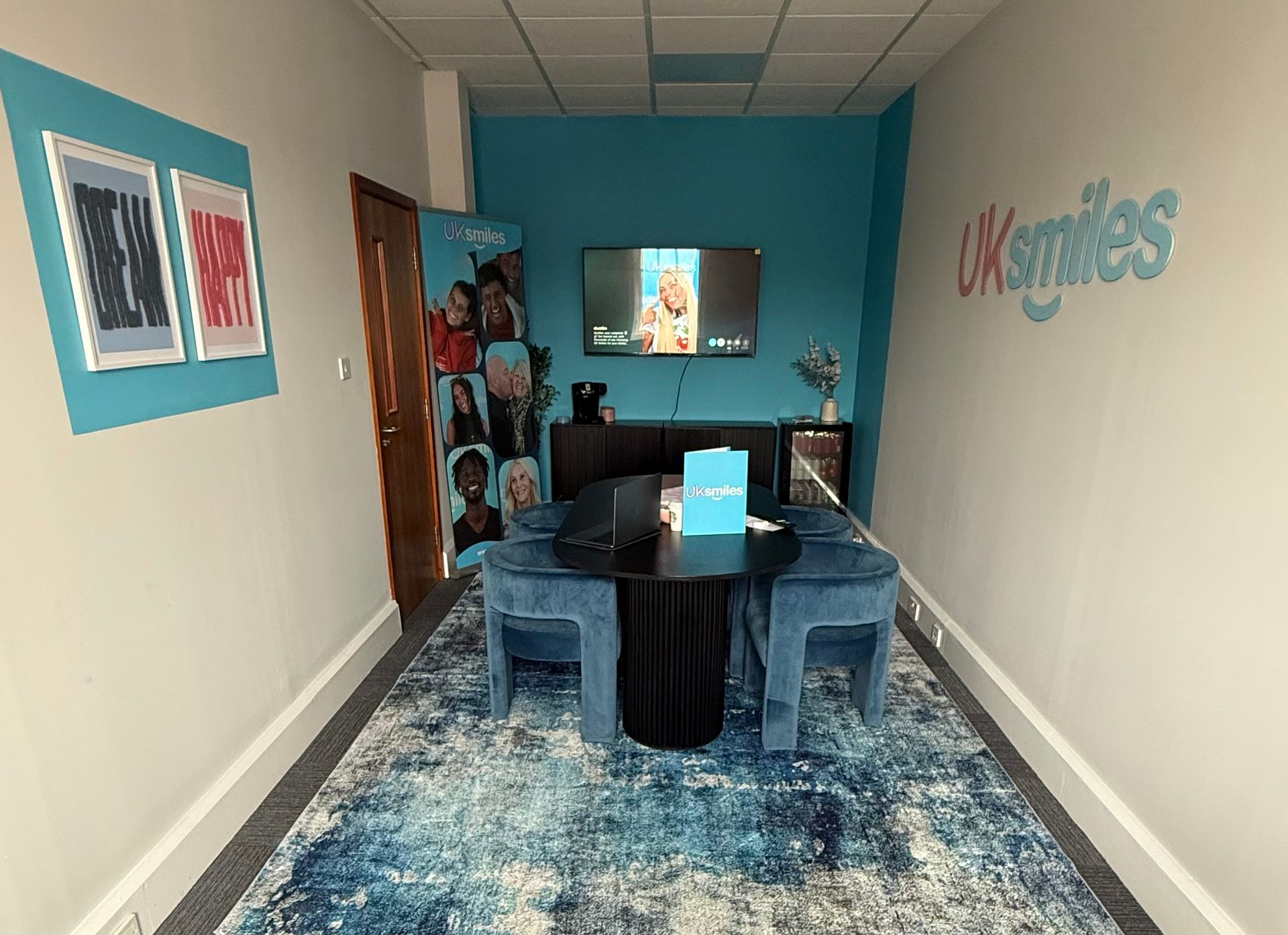A consultation room for UK Smiles. Blue and white decor with table, chairs, TV, and promotional displays.