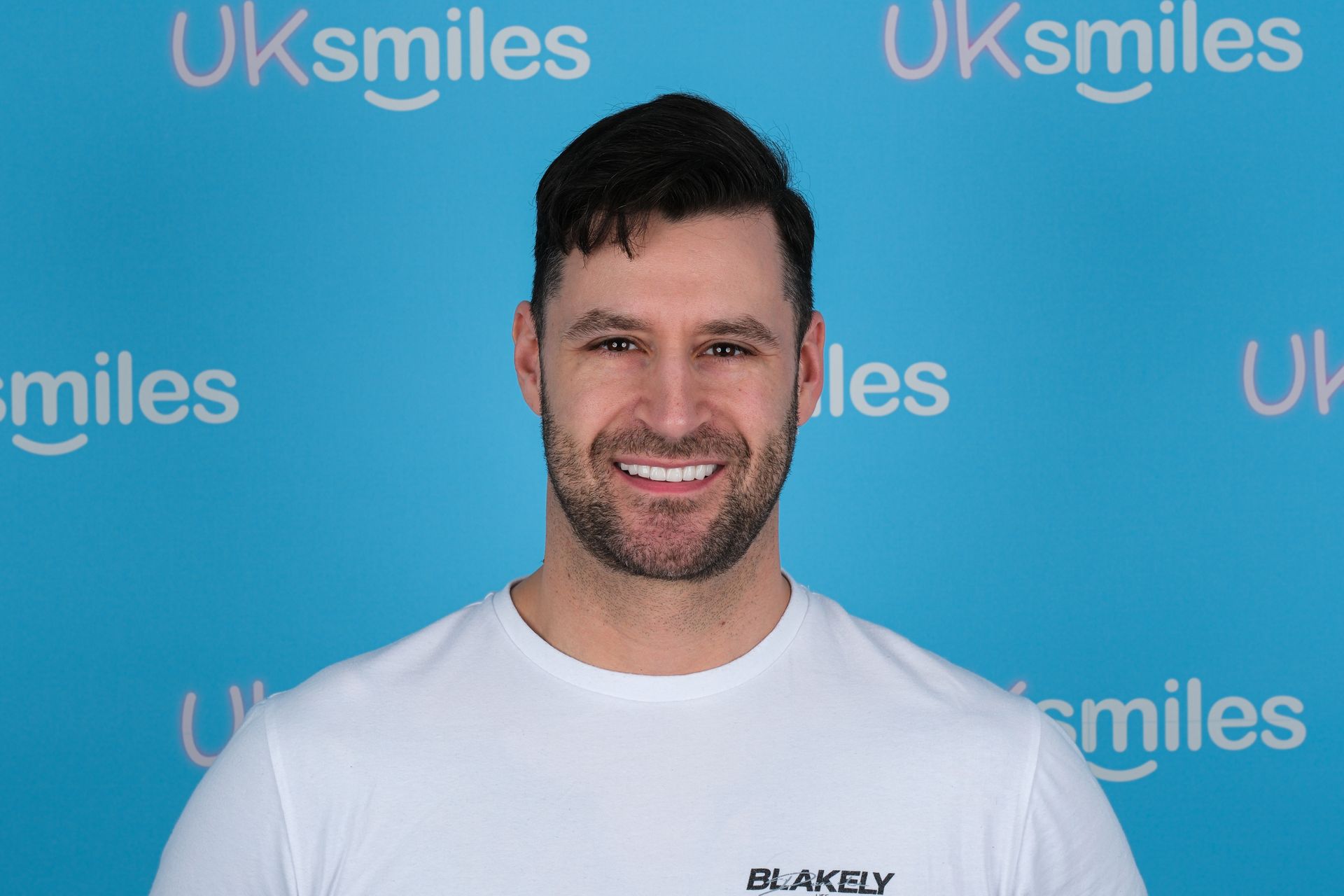 Man with a bright smile posing in front of a blue backdrop with