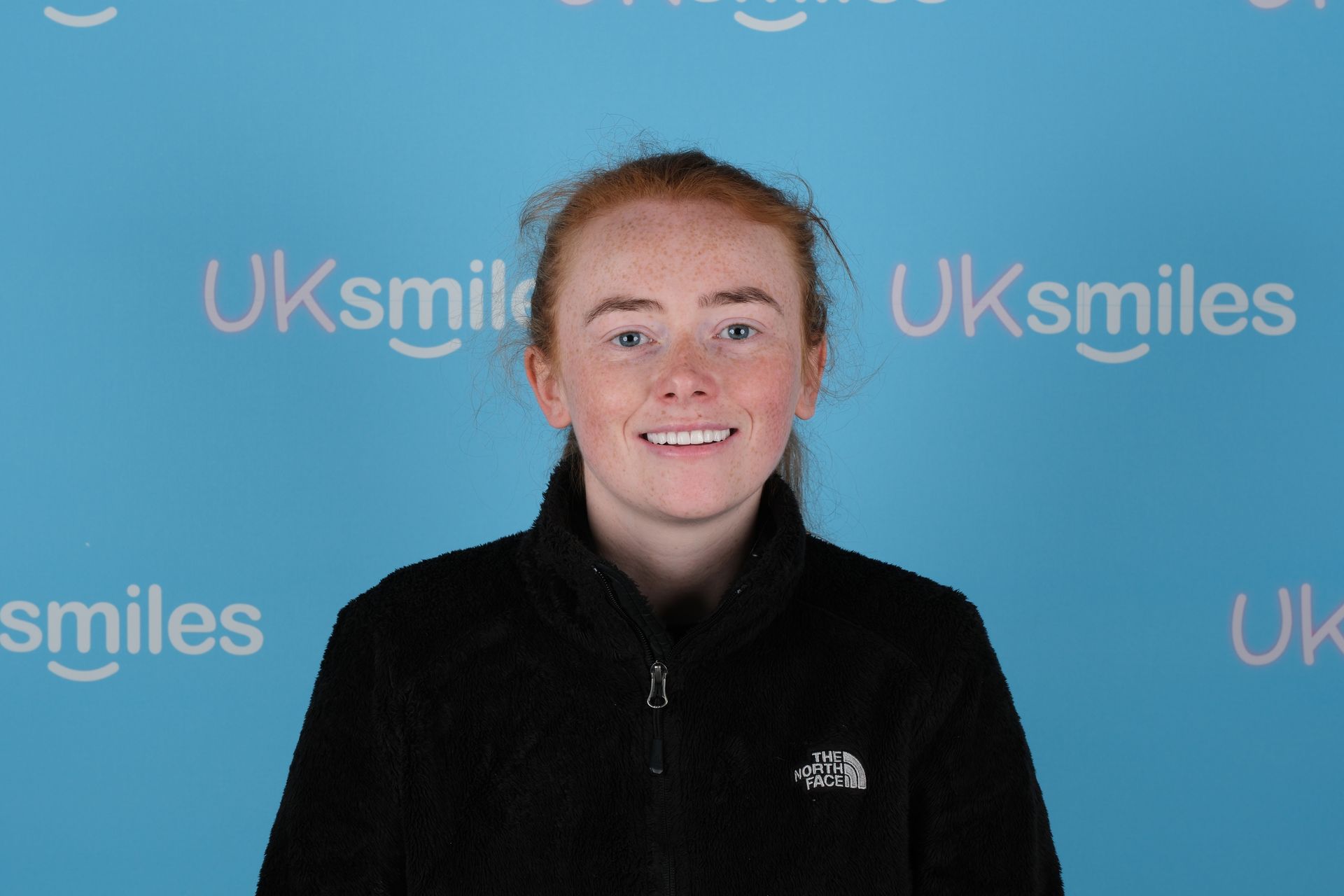 Young woman with red hair smiles in front of a blue backdrop with