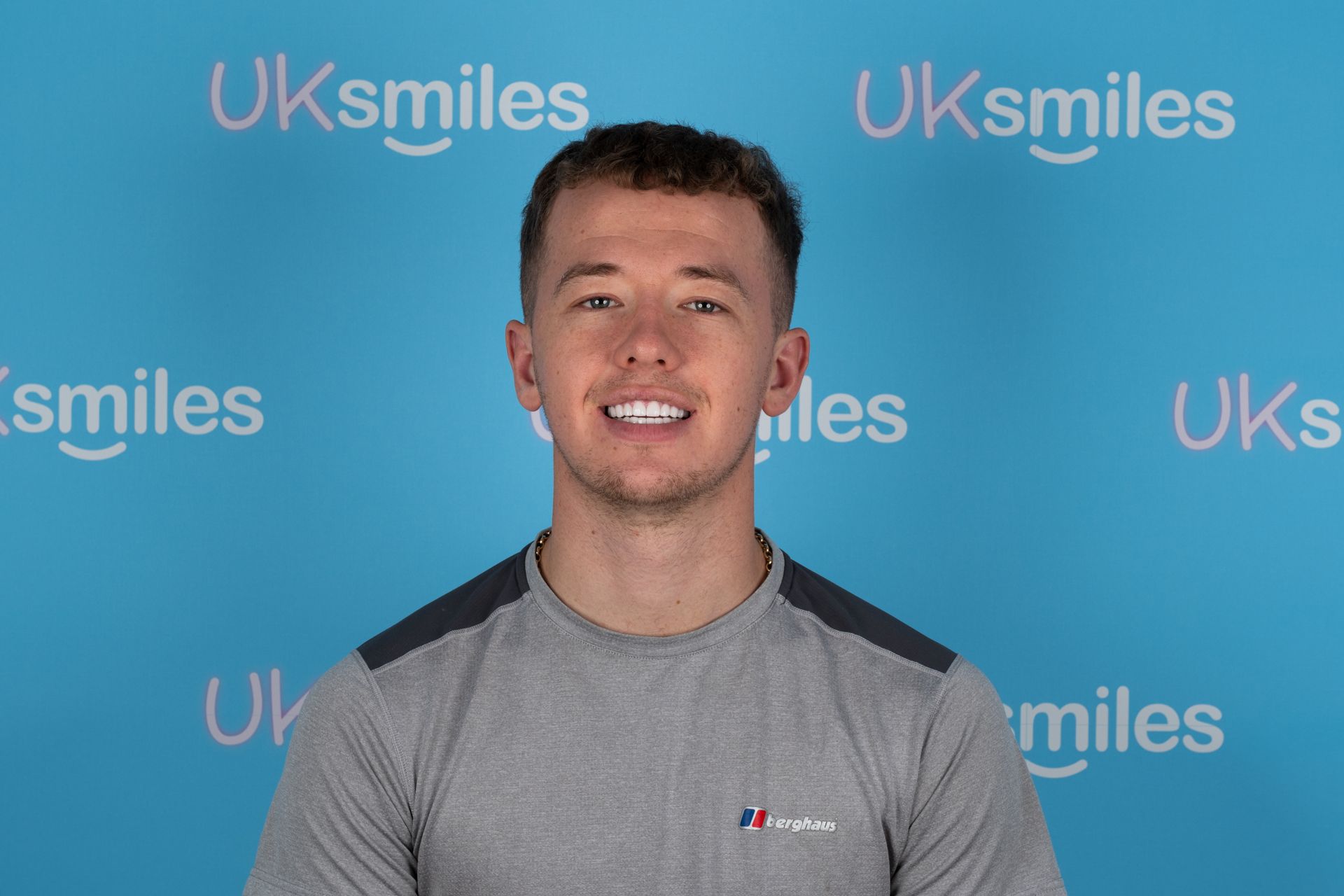 Man with a bright smile, wearing a grey shirt, against a blue background with