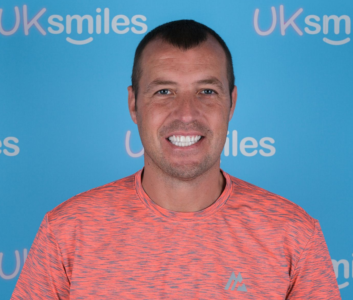 Man with bright white teeth smiles against a blue background with