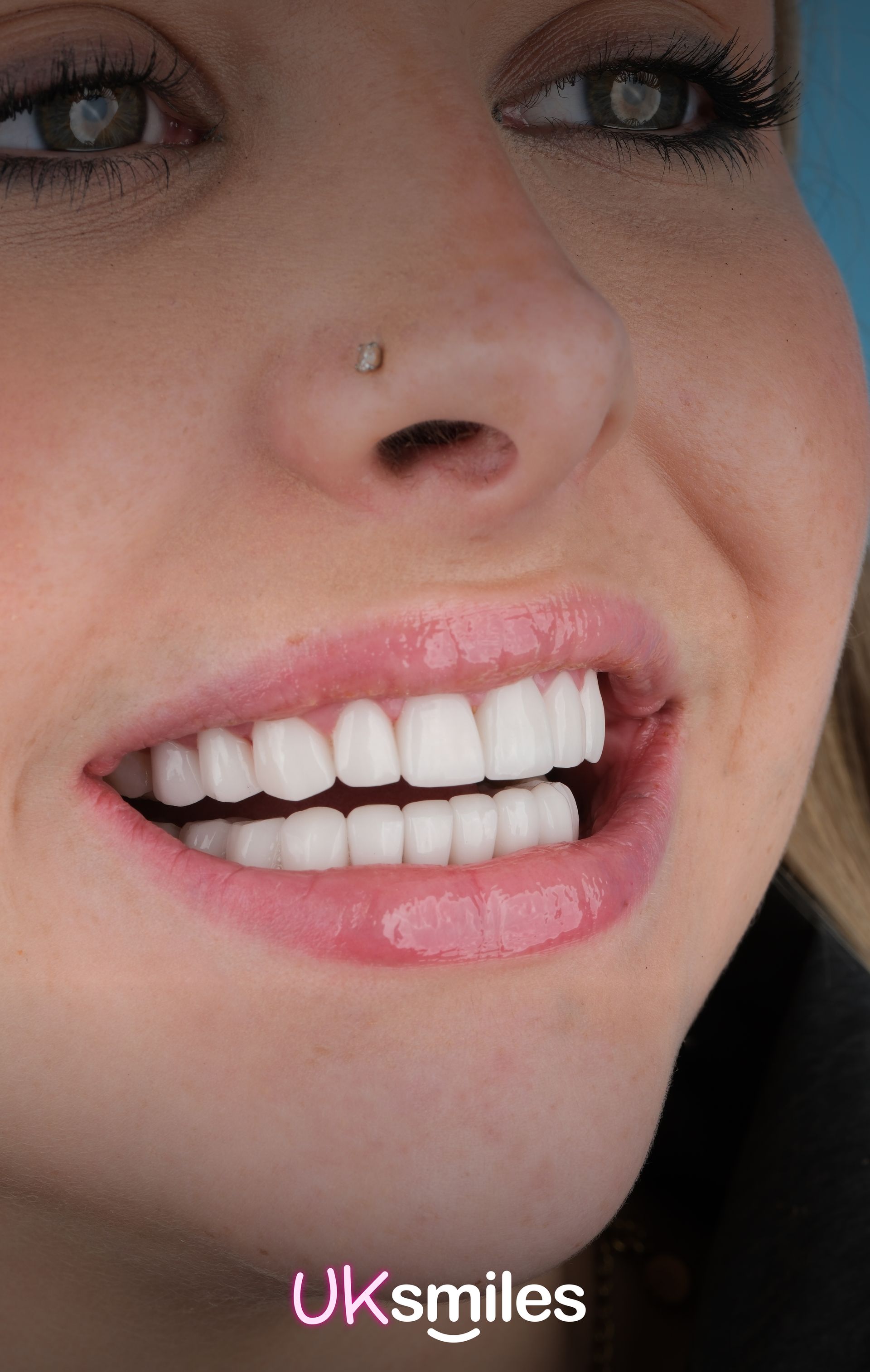Woman with bright white teeth, smiling, with a nose piercing.