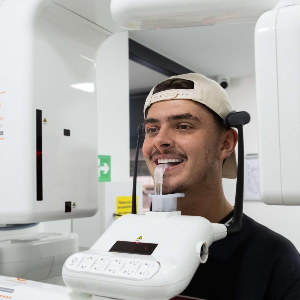 Man in dental X-ray machine, smiling, wearing a cap.