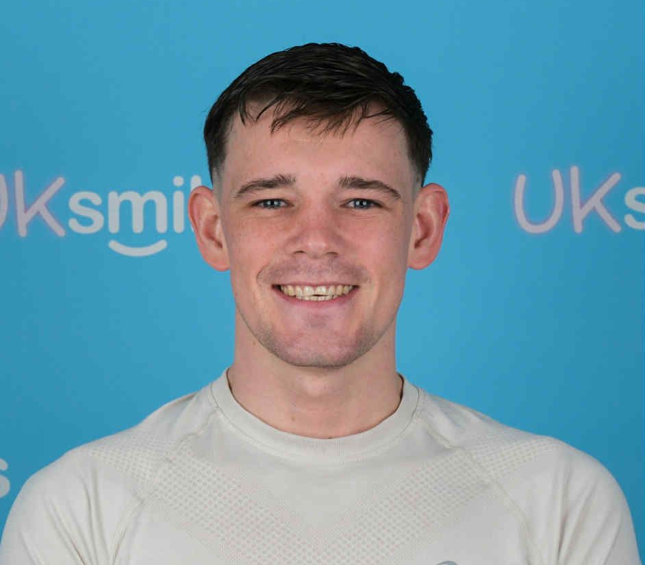 A smiling man in a light gray shirt poses in front of a blue background with a logo.