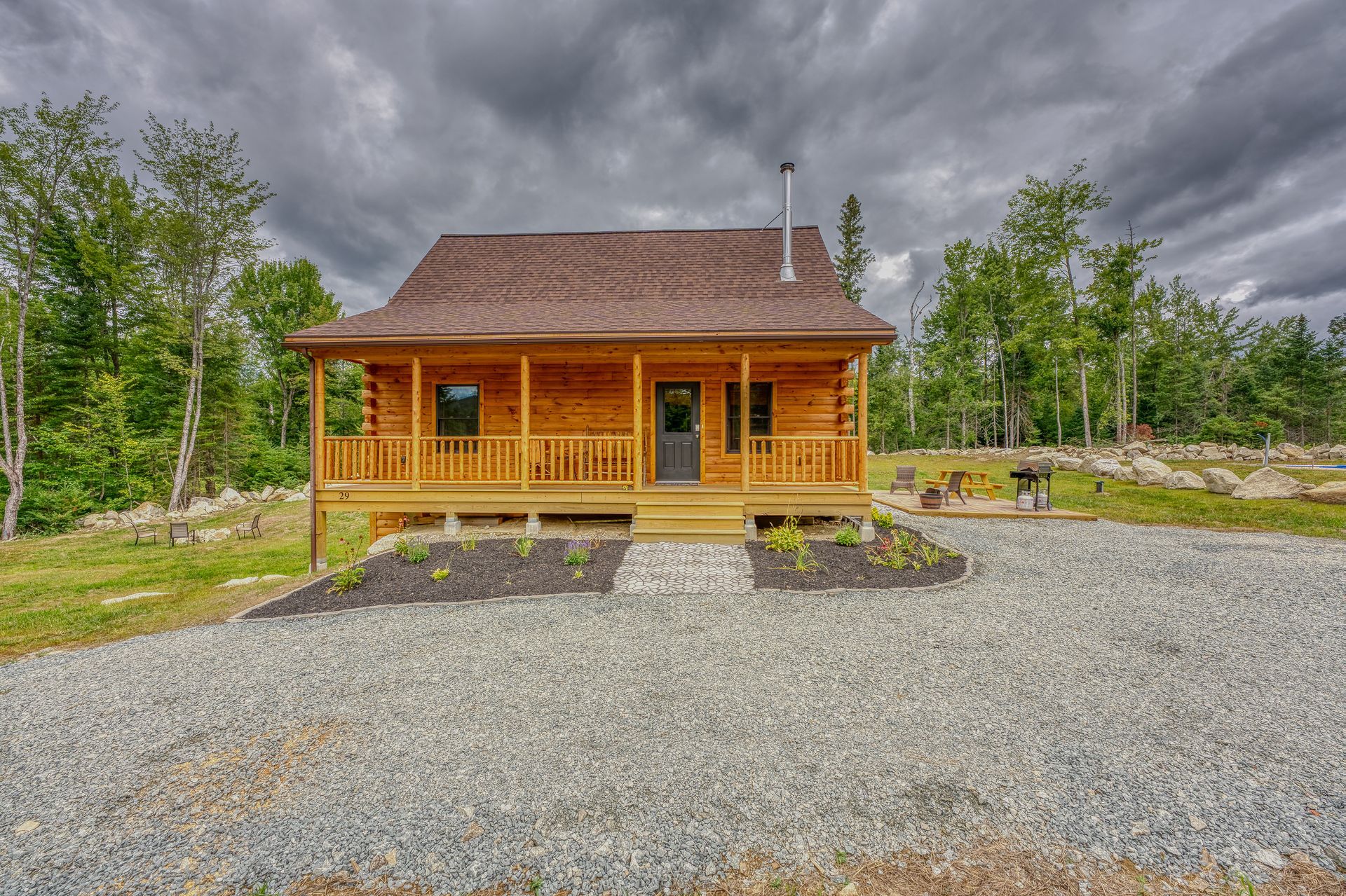 Small, wooden cabin with porch on a gravel lot, under a cloudy sky.