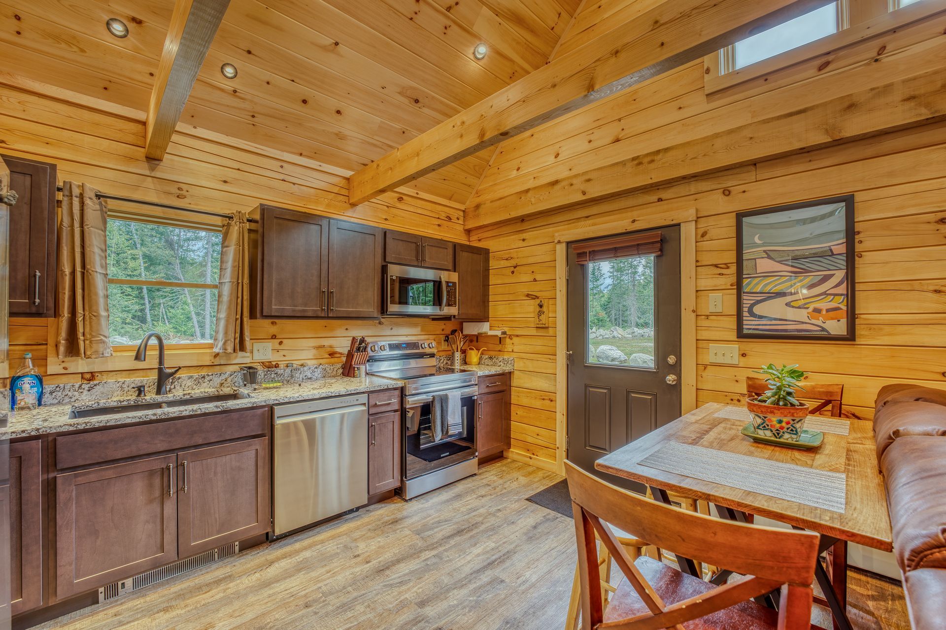 Cozy cabin kitchen with wooden walls, brown cabinets, stainless steel appliances, and a small table.