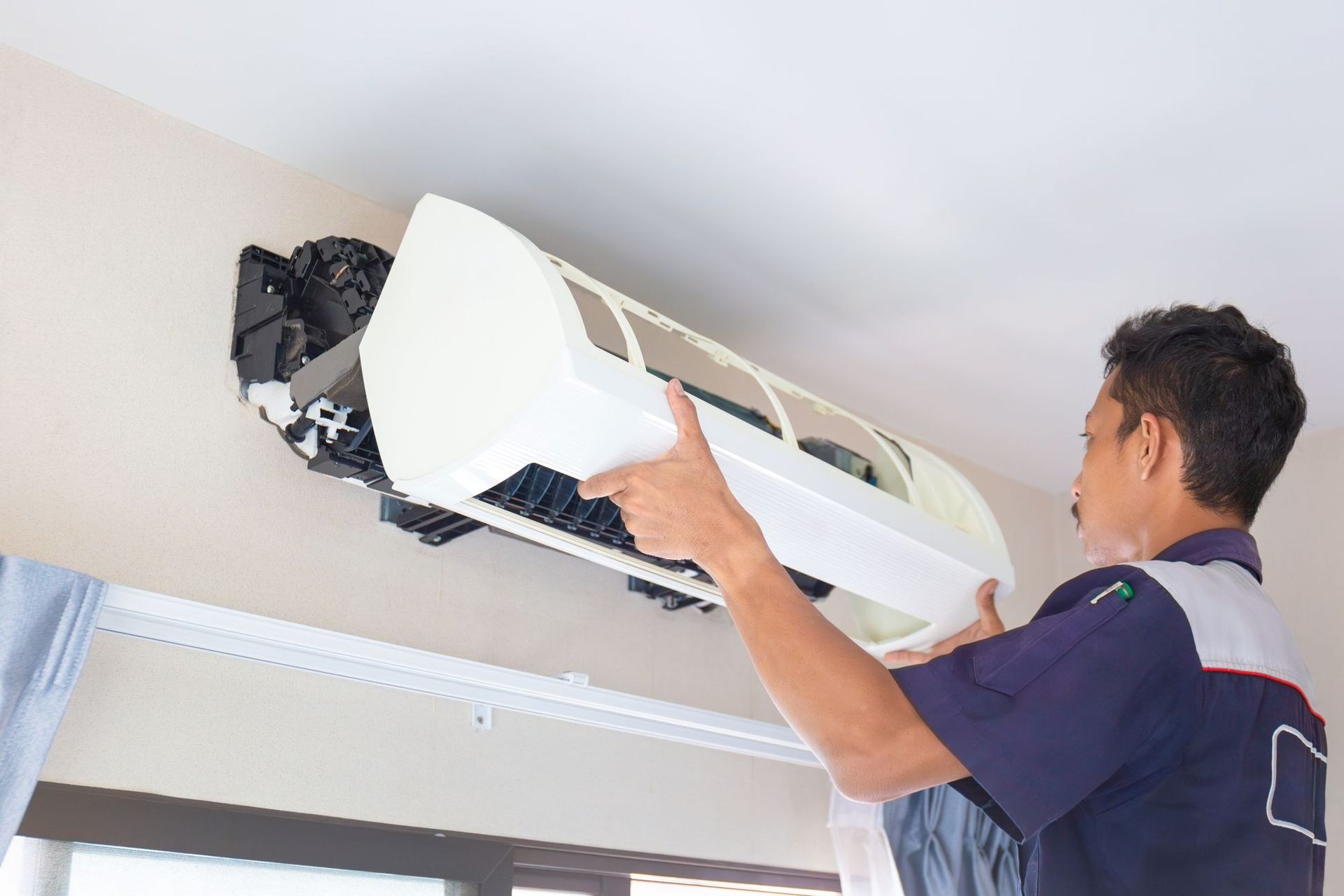Technician installing a white wall-mounted air conditioner near the ceiling
