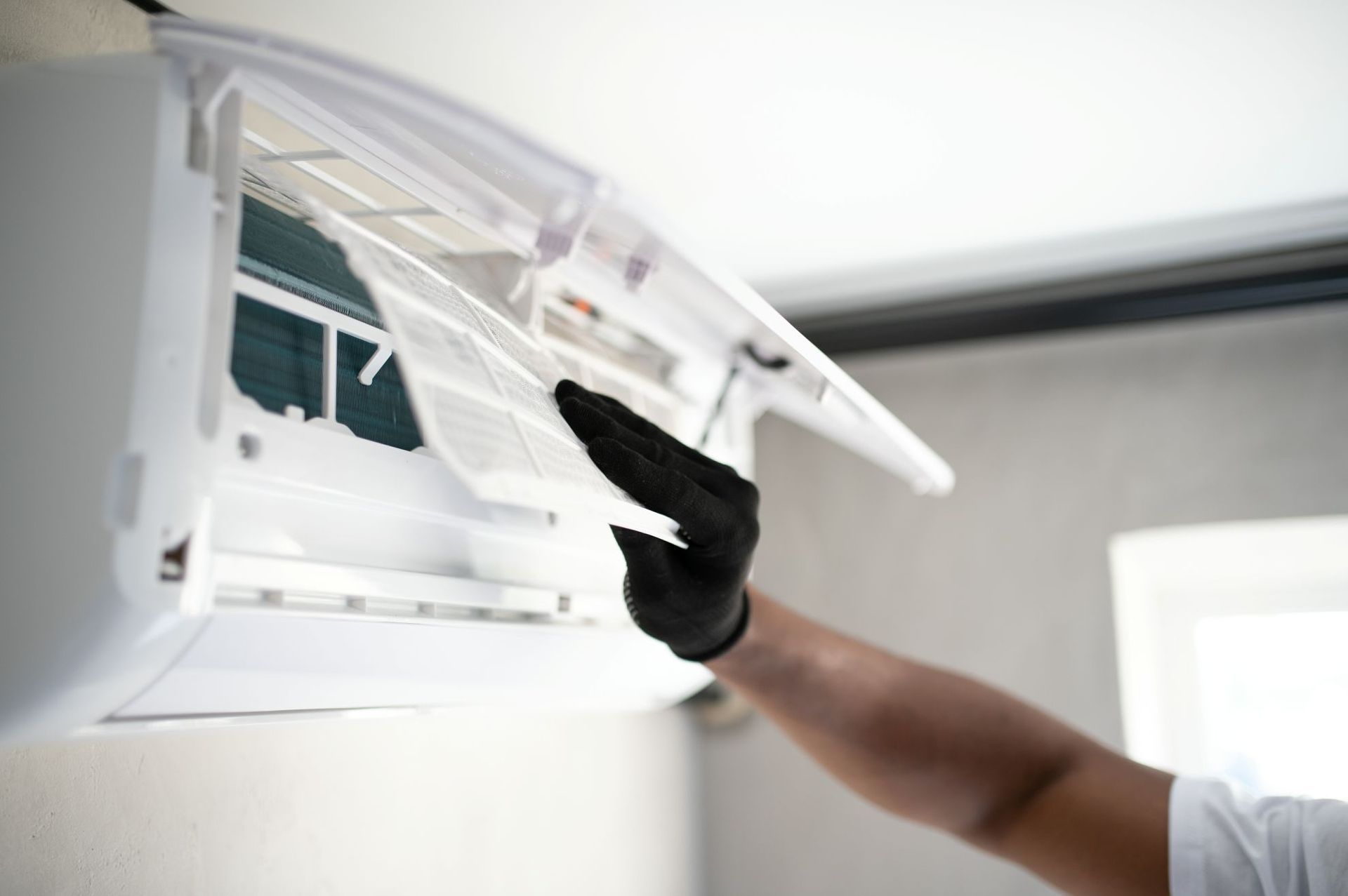 Person wearing black gloves cleaning a wall-mounted air conditioner with a cloth