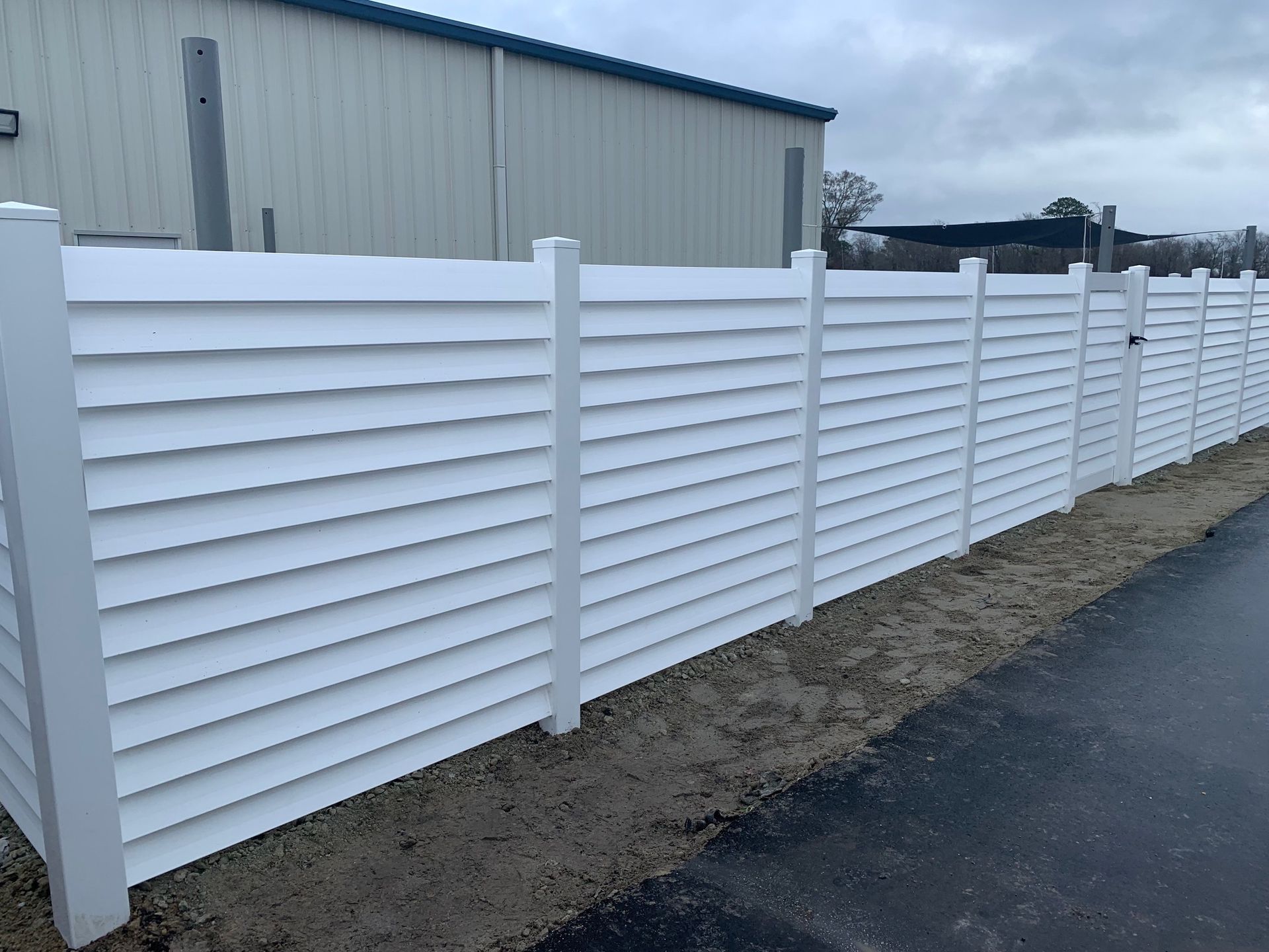 White horizontal slat fence in front of a building on a cloudy day.
