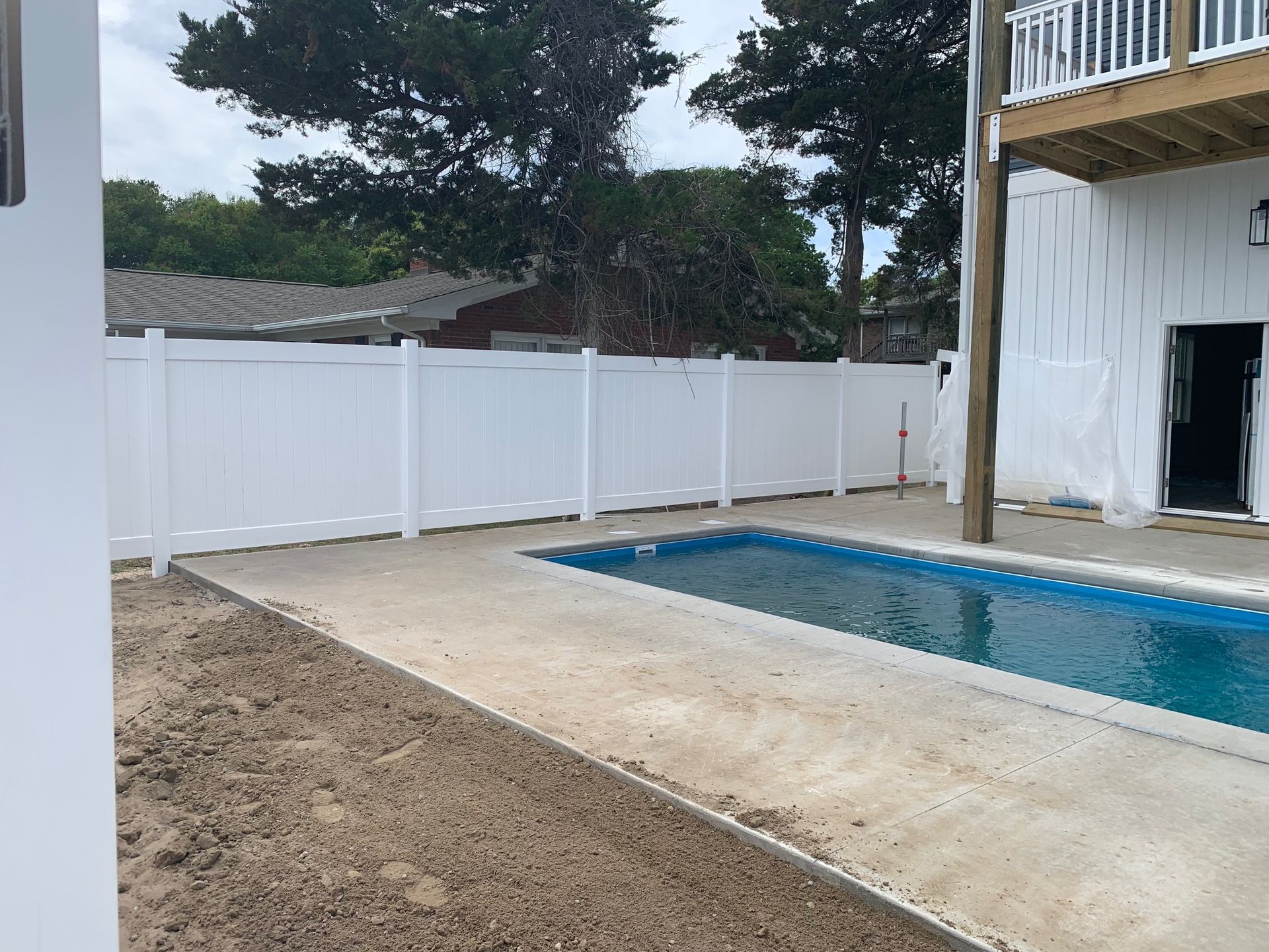 Pool with white fence, next to a white building with a balcony, under a cloudy sky.
