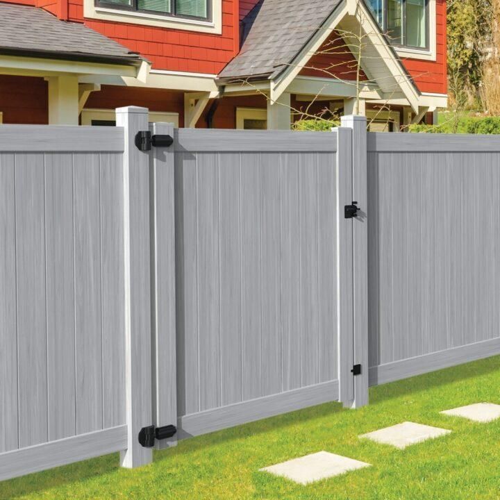 Gray vinyl fence with gate in front of a red house on a green lawn.