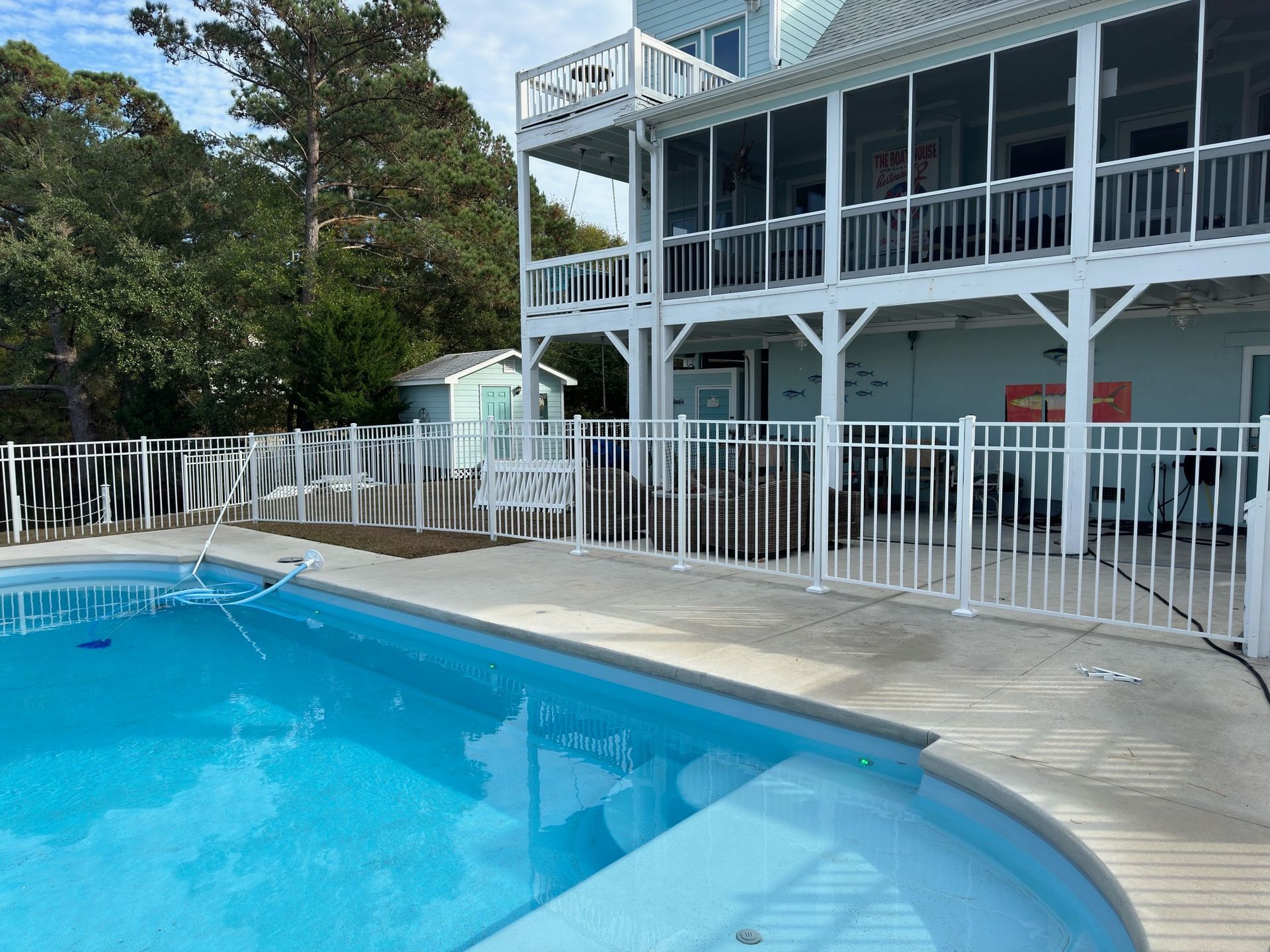 white fenced yard in front of a light blue house with porch and deck, under a cloudy sky.