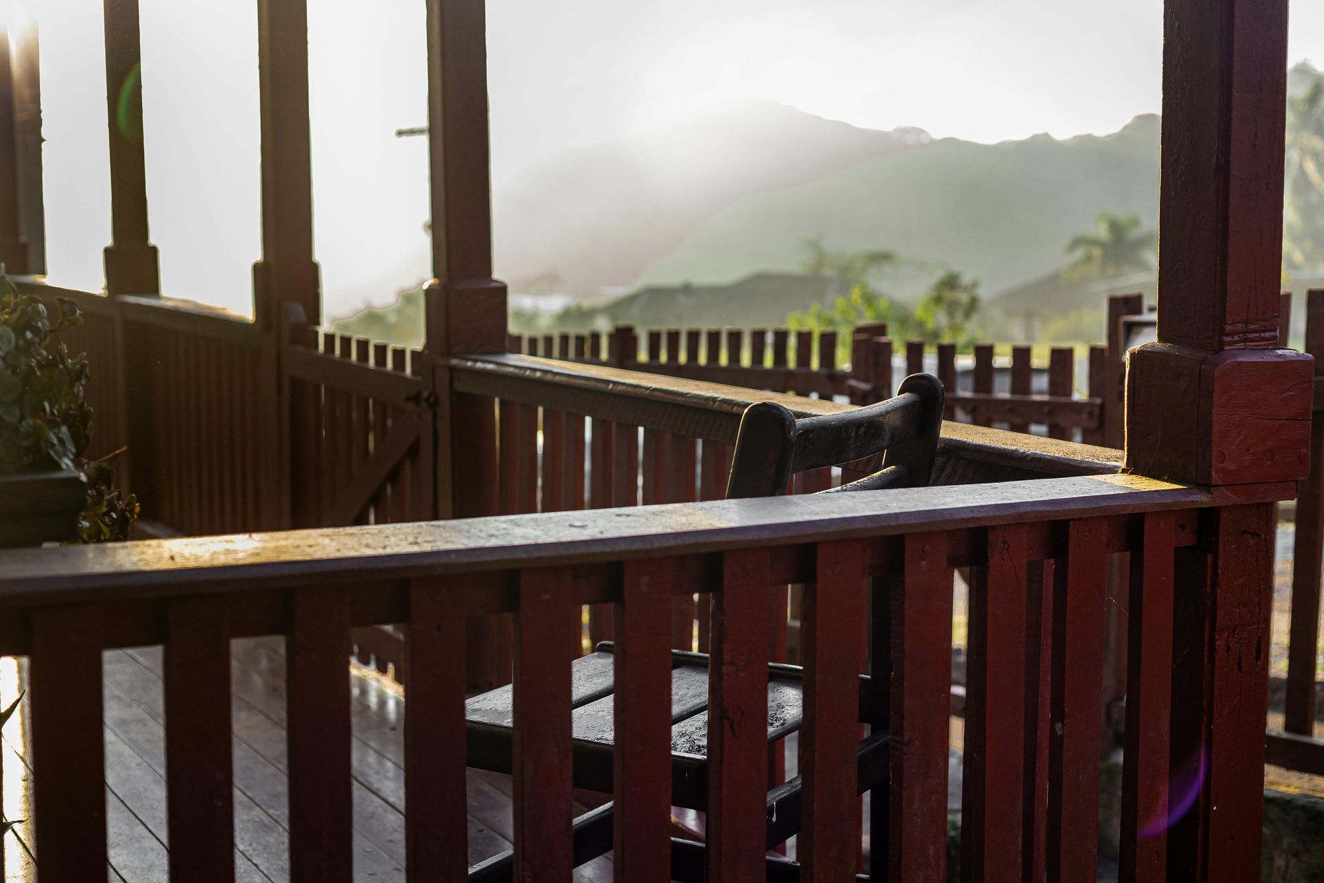 Wooden deck with red railing, overlooking a mountain range on a sunny day.
