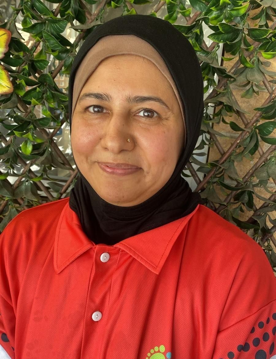 A woman wearing a hijab and a red shirt is standing in front of a tree.