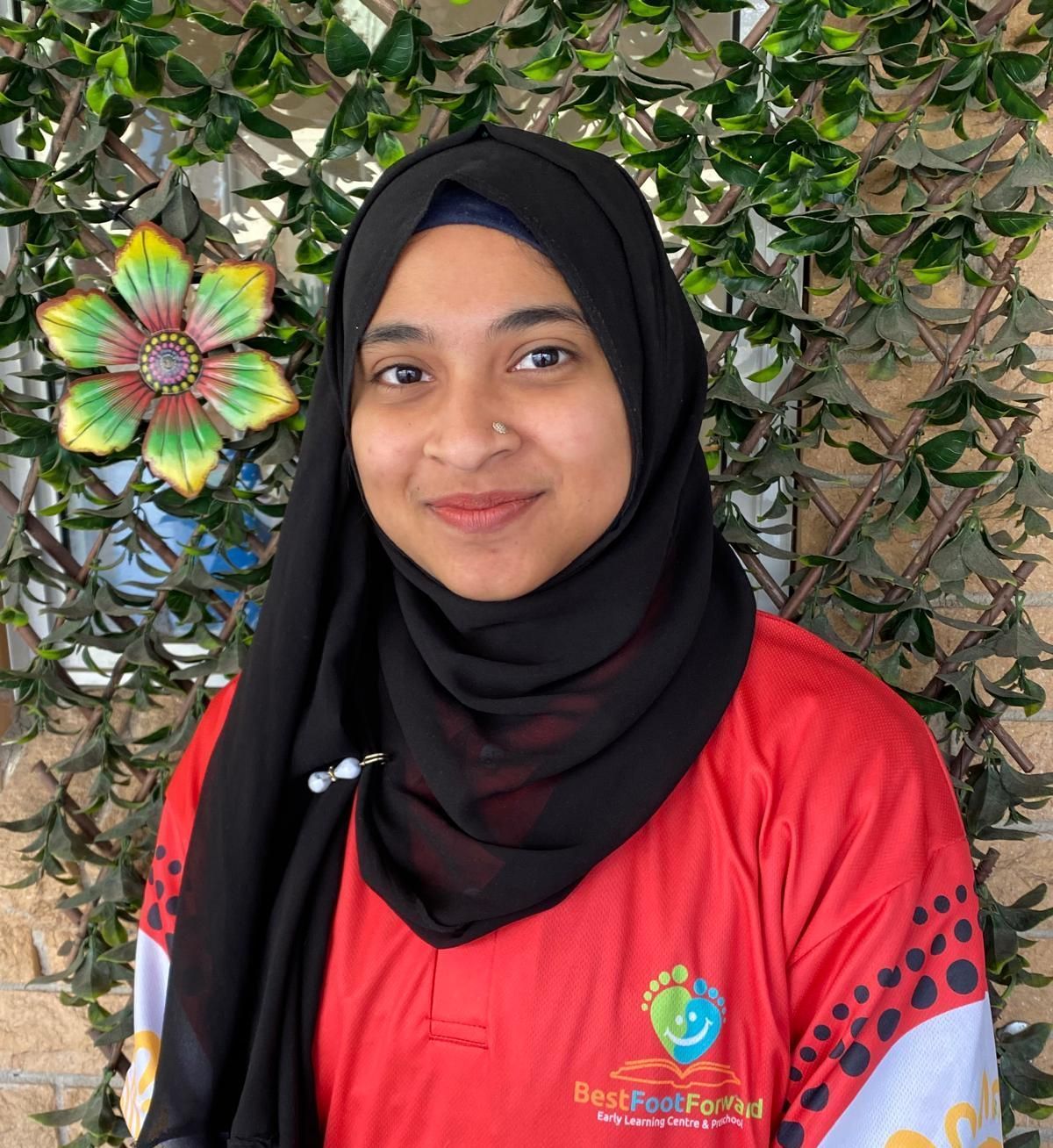 A woman wearing a hijab and a red shirt that says best foot forward