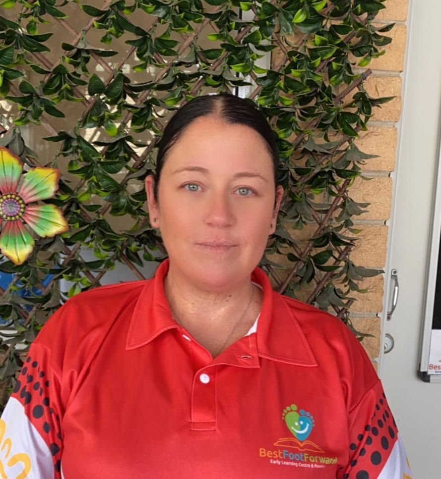 A woman educator in a red shirt is standing in front of a fence.