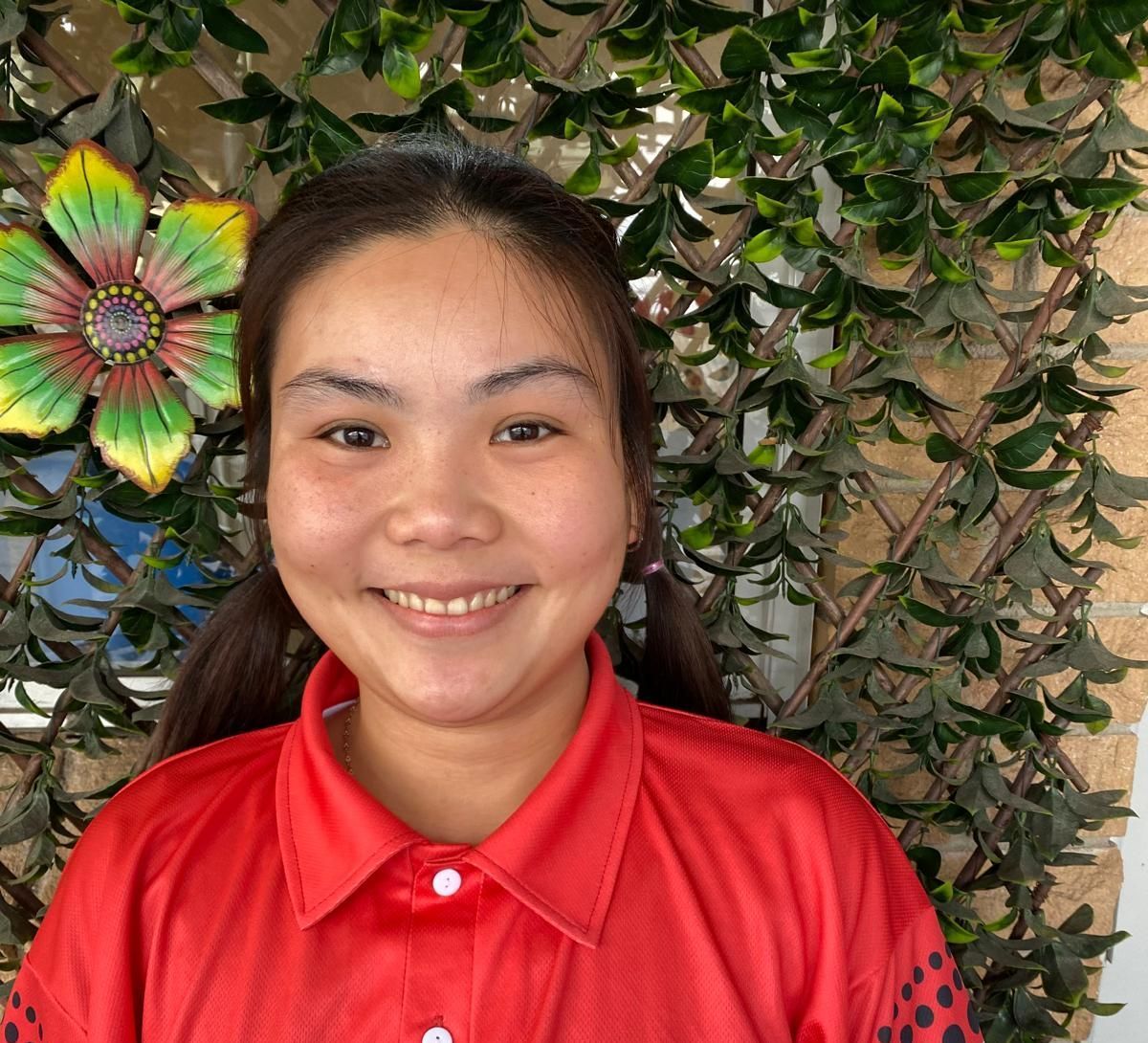 A woman in a red shirt is smiling in front of a flower