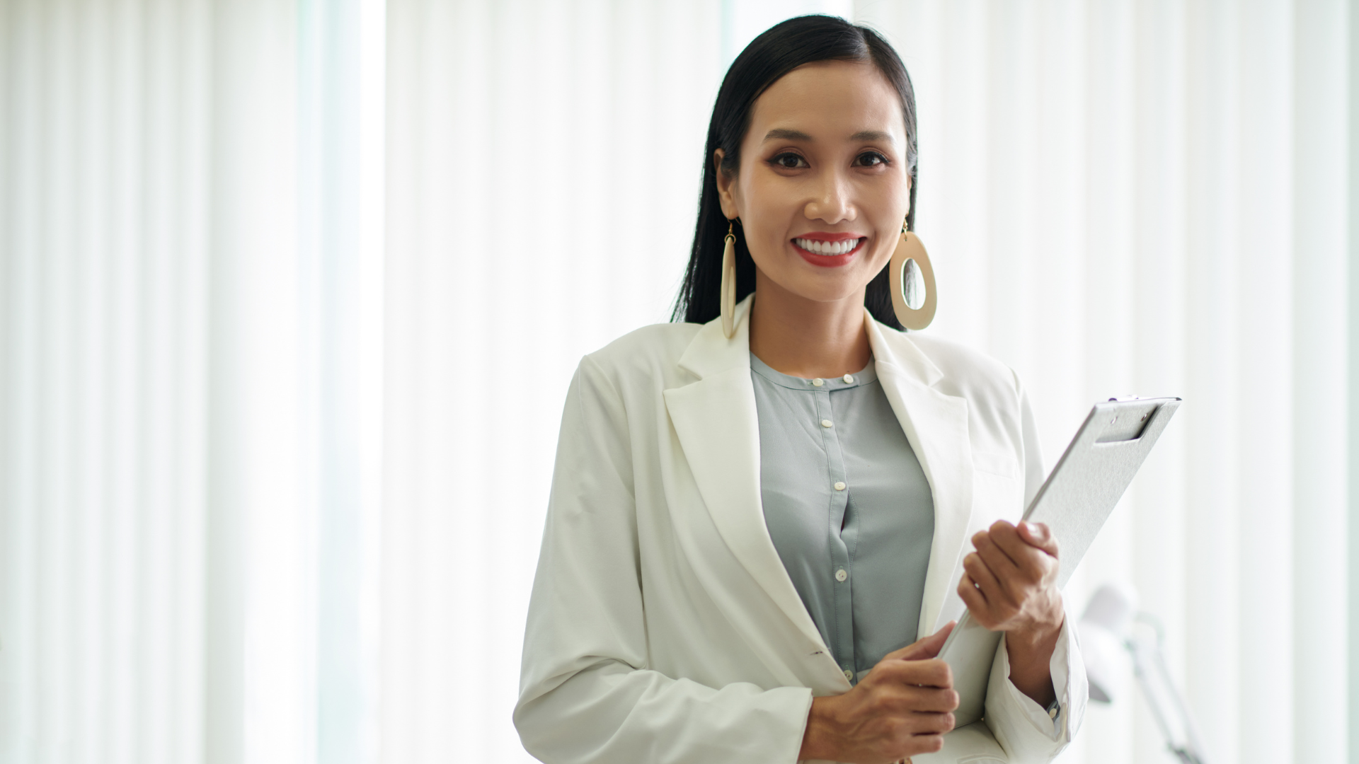 Woman on sofa using laptop in office; colleagues work at desks.