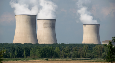 Three large, cylindrical cooling towers emitting steam over a treeline, likely a nuclear power plant.