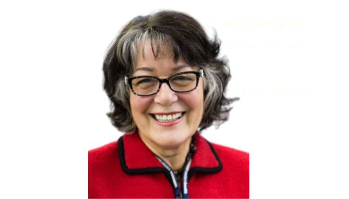 Woman with glasses smiling, wearing a red jacket with a white and blue zipper, outdoors.