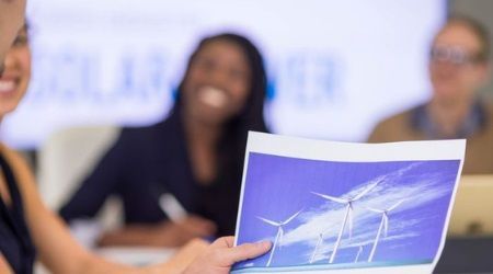 Person holds document with wind turbines, smiles, in business meeting with colleagues.