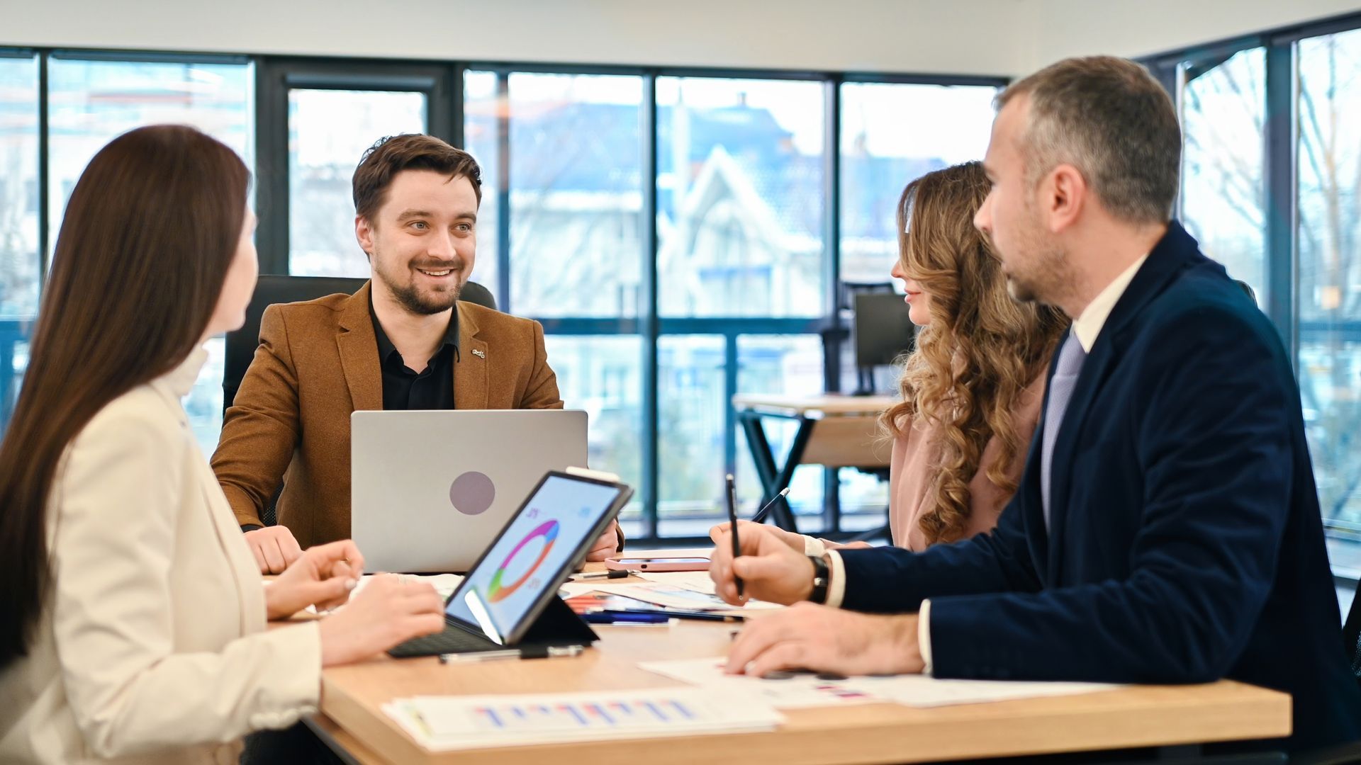 Four business colleagues in a meeting, analyzing data with a laptop and tablet, inside office.