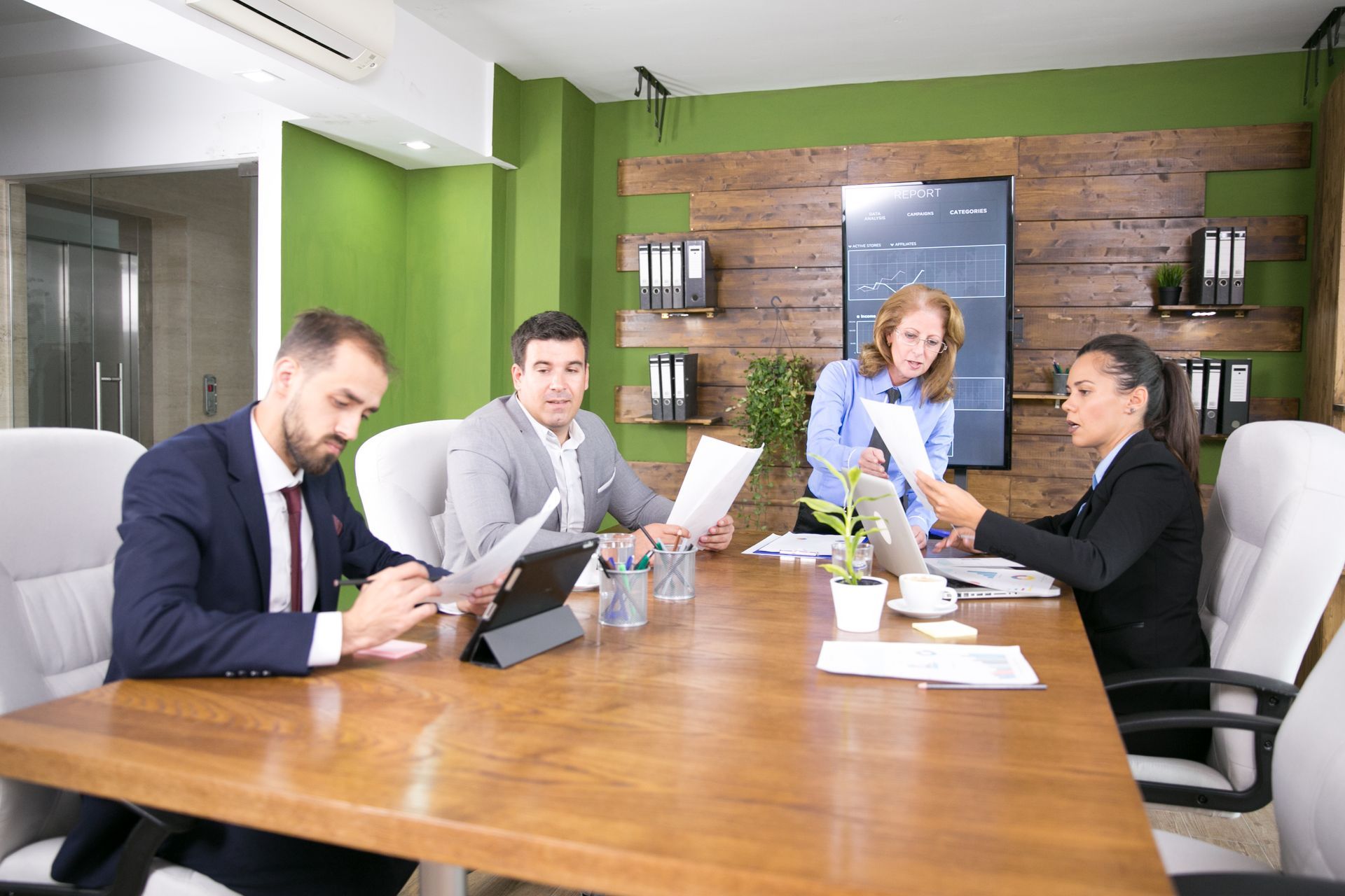 Business meeting in a modern office with four people reviewing documents around a large wooden table.