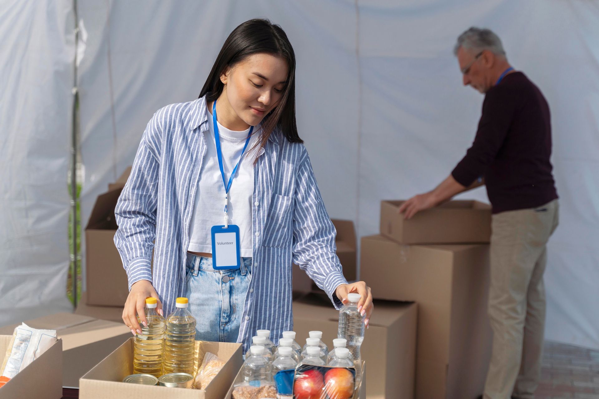 Woman and man sorting food donations into boxes inside a tent.