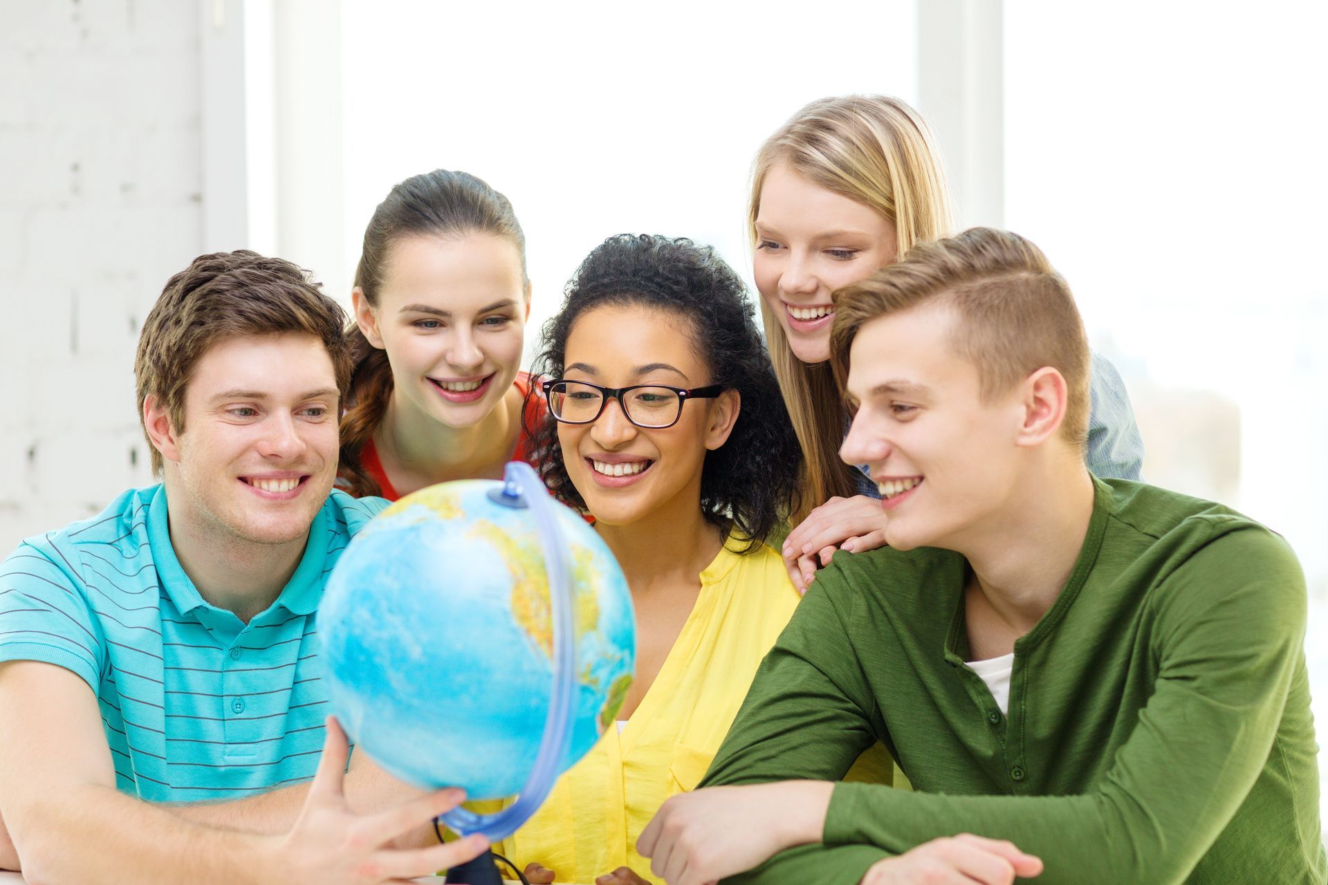 Five students gather around a globe, smiling, indoors.