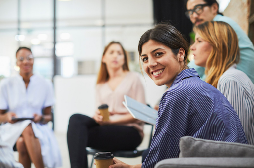 Three people looking at laptop screen, man pointing, smiling. Office setting.